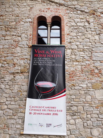 banner for Vine & Wine Rossi Nativi hanging from romanesque double-arched window high on stone wall