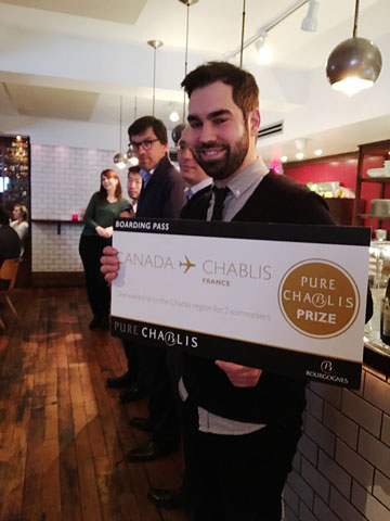 he's holding a big 'boarding pass' for a Canada-Chablis flight; it's labelled PURE CHABILS PRIZE