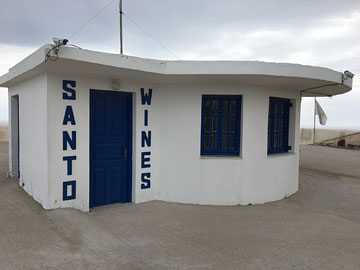 small white building with blue doors and shutters and SANTO WINES vertically on either side of the door in blue